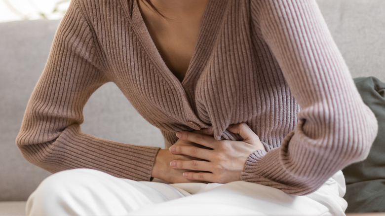 Woman sits on couch holding stomach in pain