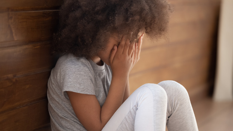Young child sits on floor with face in hands sadly