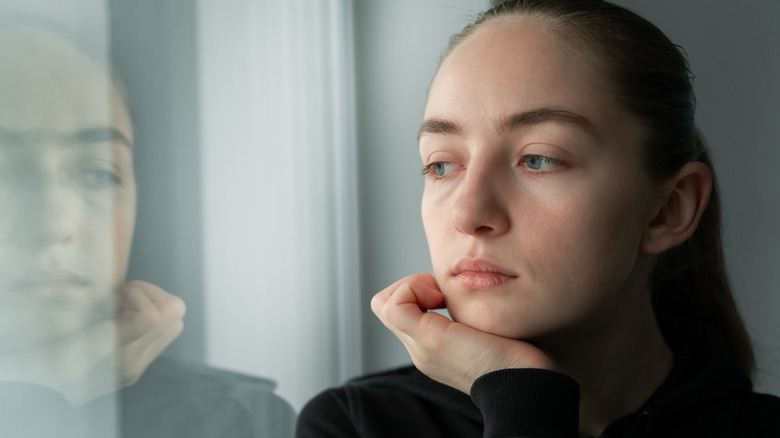 Woman at home looks out the window sadly