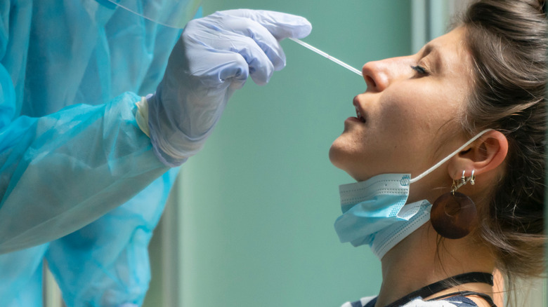 Healthcare worker with protective equipment performs COVID-19 swab test on woman