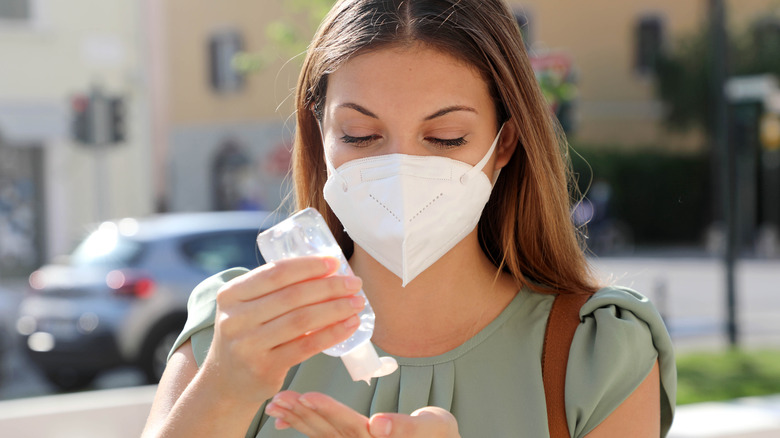 Woman with KN95 FFP2 mask using alcohol gel sanitizer hands in city street