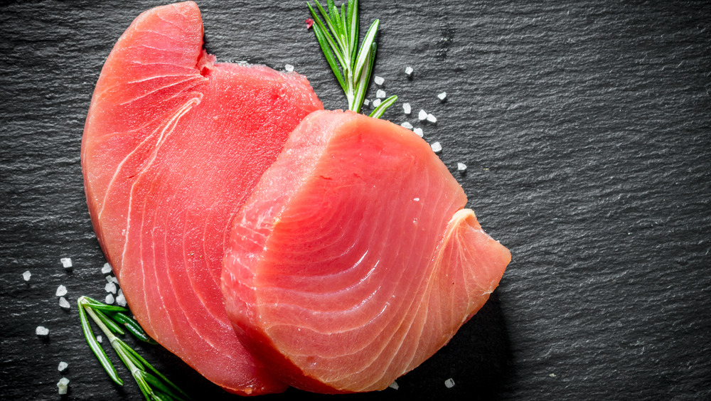 Fresh raw tuna filets on garnished with rosemary and salt on a black slate background