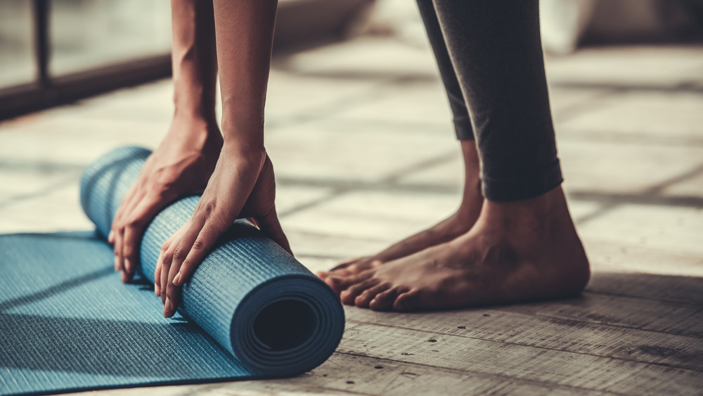 Close up of woman's hands and feet rolling out a yoga mat