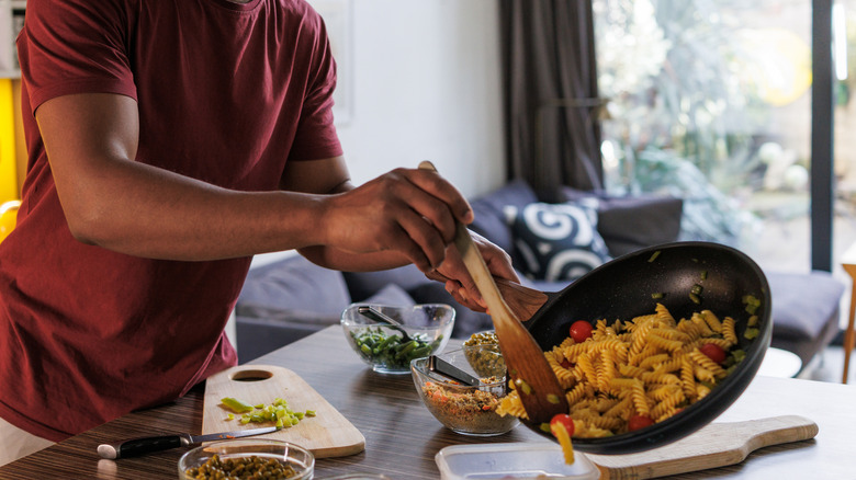 man putting pasta into container in kitchen