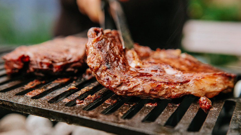 A hand barbecuing steaks on a grill