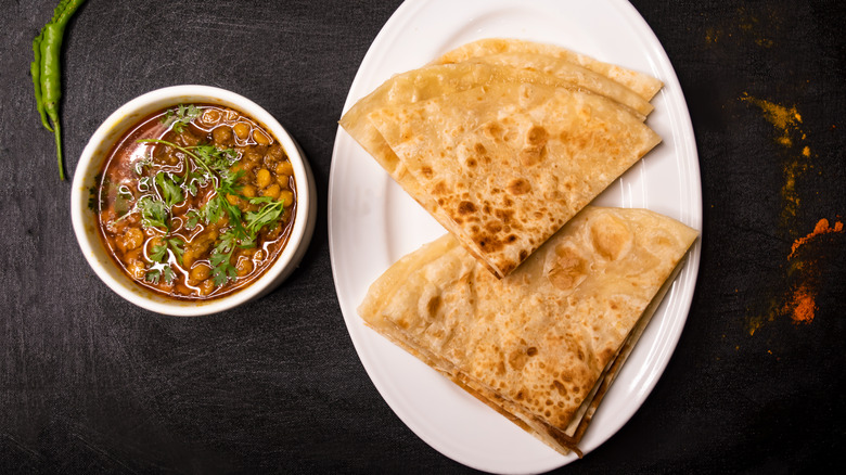 A high-angle shot of a bowl of dal next to a plate of naan