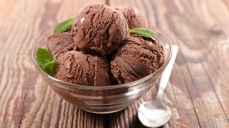 A glass bowl of several scoops of chocolate ice cream and a spoon
