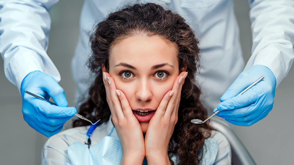 Woman holding hands on face with dentist behind her