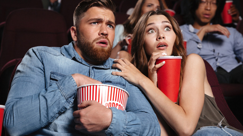 Couple eating popcorn at movie theater reacting to scary movie
