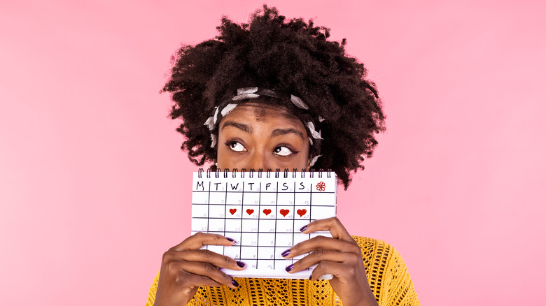 a young black woman holding a calendar with her period marked by hearts