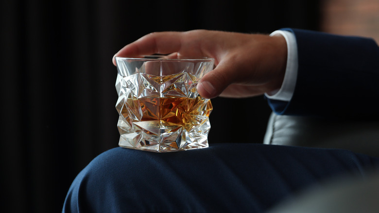man resting glass of scotch on knee