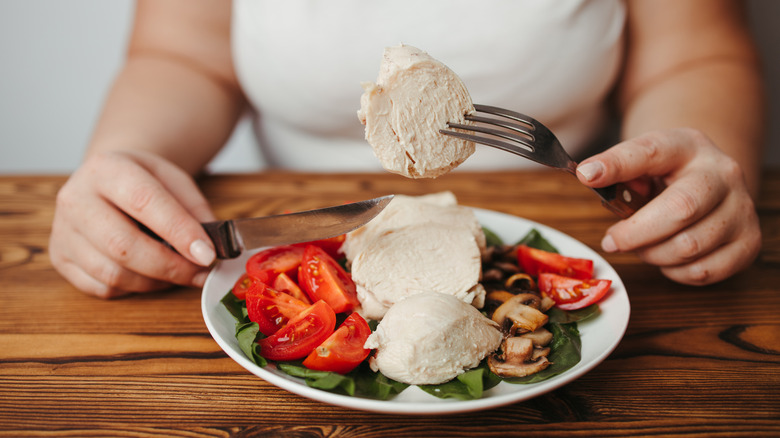 A woman eating chicken breast, tomatoes, mushrooms, and greens