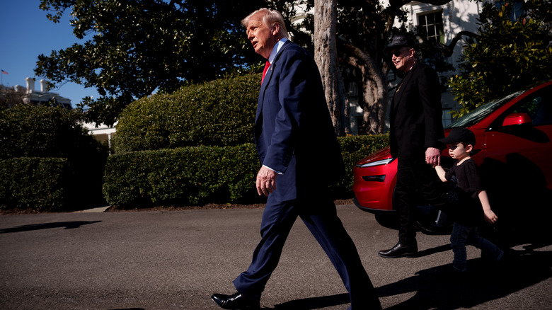 Side profile shot of President Donald Trump walking with Elon Musk and his son outside.