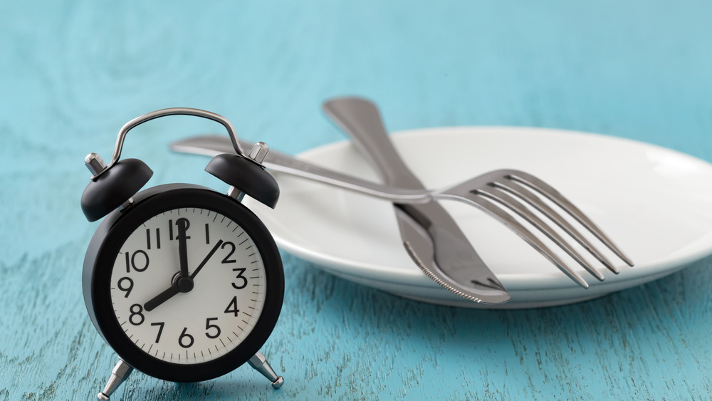 Intermittent fasting. White plate with fork and knife and alarm clock.