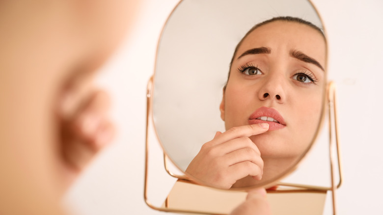 Woman looking in a mirror at cold sore on her lip 
