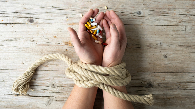 hands holding pills tied by rope