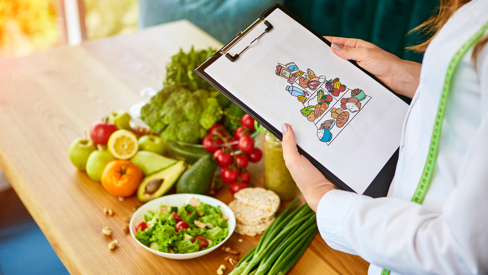 Dietitian holding a clipboard in front of table of fruits and vegetables