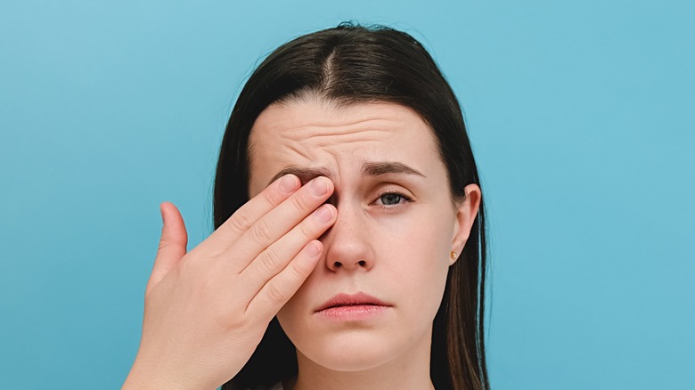 woman with furrowed brow holding her eye