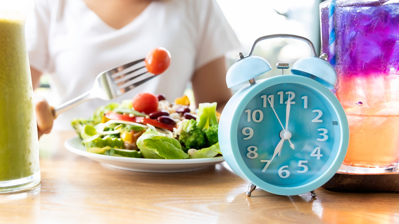 woman eating salad next to clock