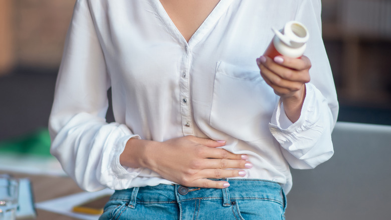 woman touches stomach while checking medicine