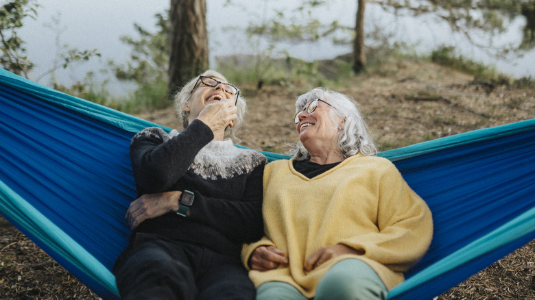 Two older women laughing while on a hammock