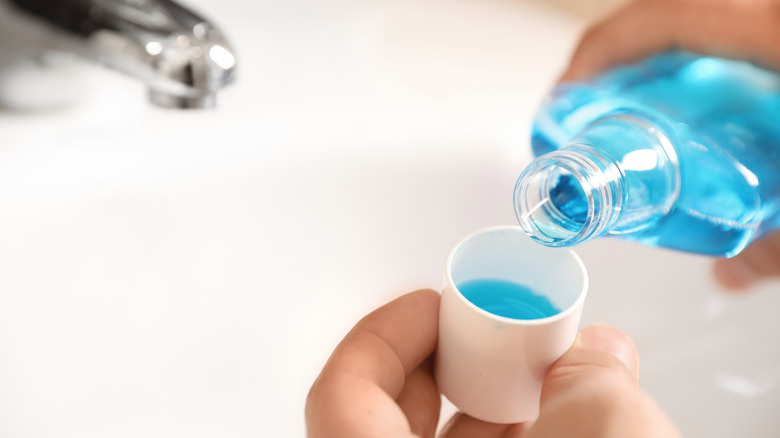 Someone pours mouthwash in a cup