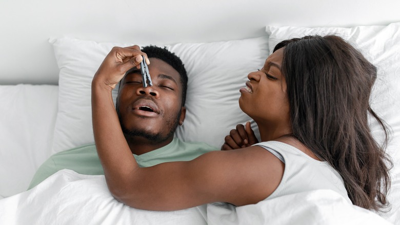 a woman tries to hold mans nose as he snores 