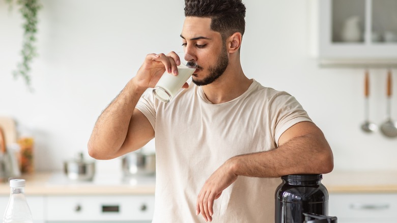 man drinking a protein shake next to a tub of protein powder