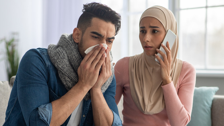 Man holding tissue to his nose next to worried woman