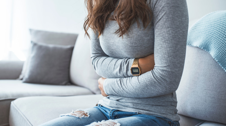 Close-up of woman on the couch holding her abdomen in pain