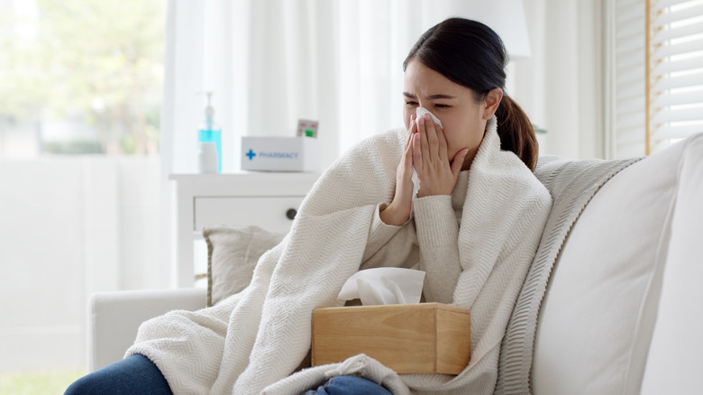 Woman on couch blowing nose