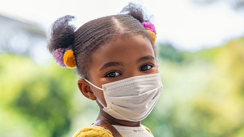 Smiling little girl with school backpack and protective face mask 