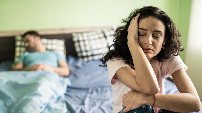 upset woman on bed in front of sleeping man