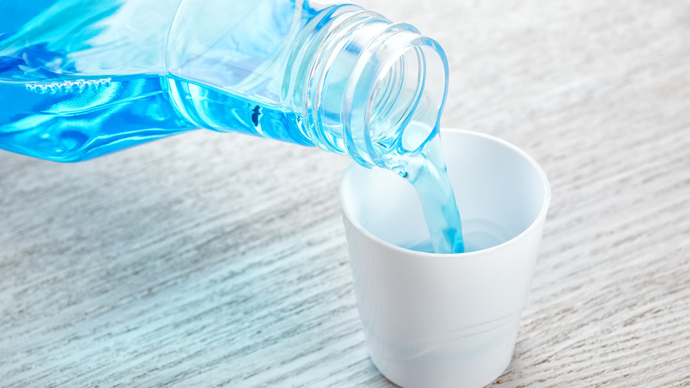 Blue mouthwash pouring from a plastic bottle into a small white cup