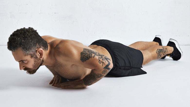 A fit man doing diamond push-ups on a white floor