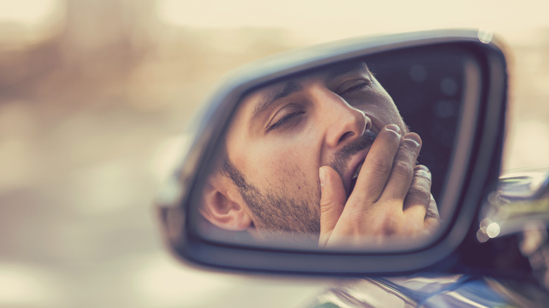 man driving and yawning in side mirror