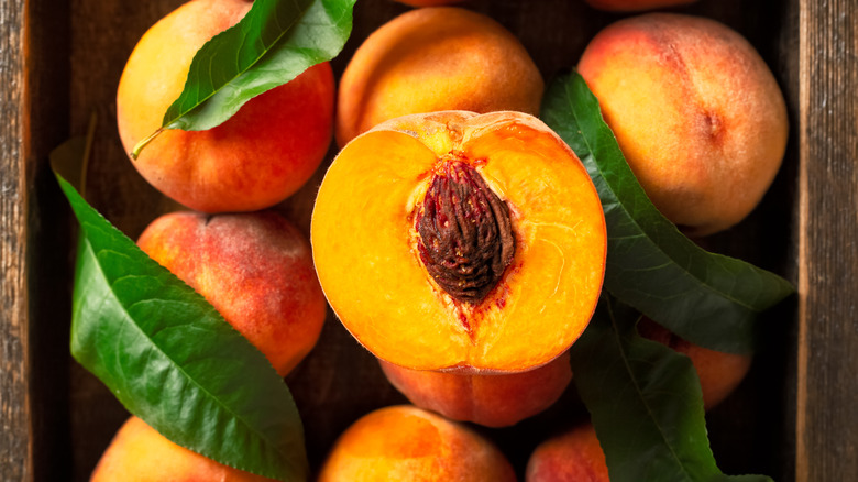 A crate of peaches with a peach on top cut in half