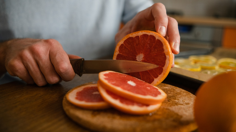 A man's hands slicing red grapefruit into small sections