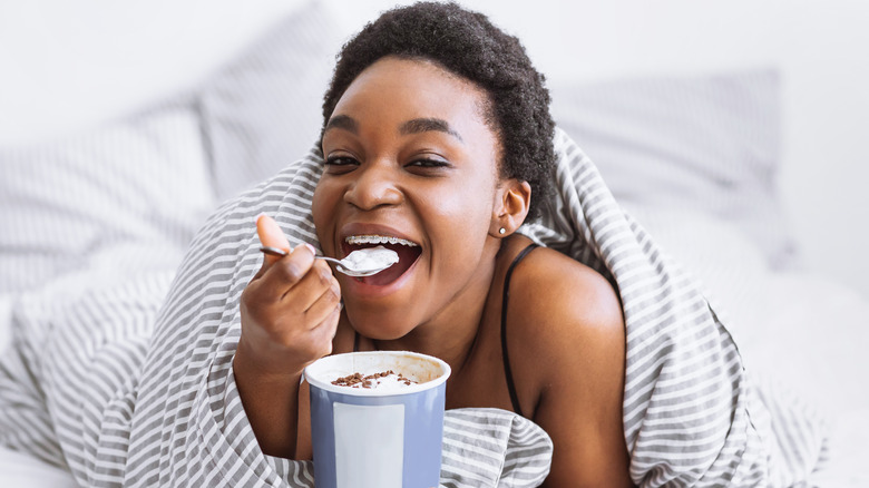 Woman mid-bite eating ice cream in bed