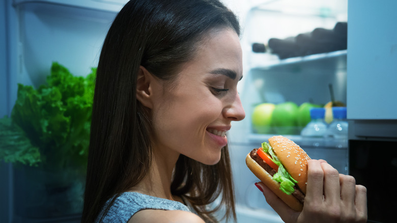 Eating burger at open fridge