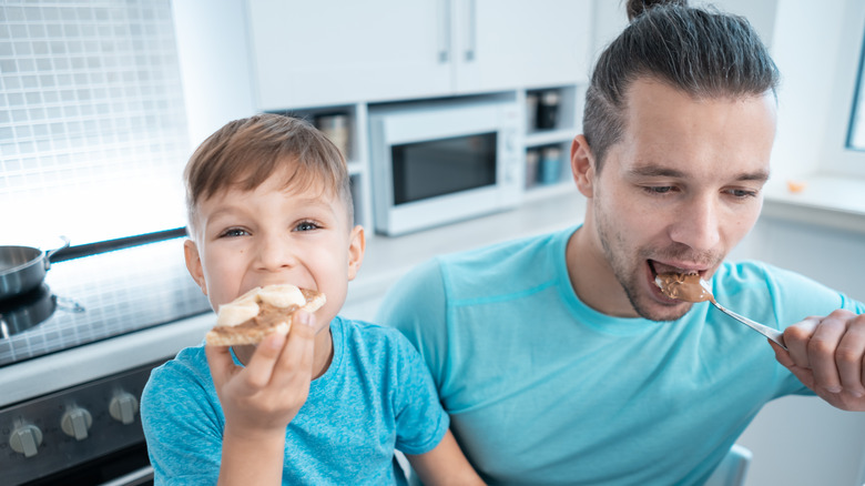 Happy kid and father eating peanut butter toast at home 