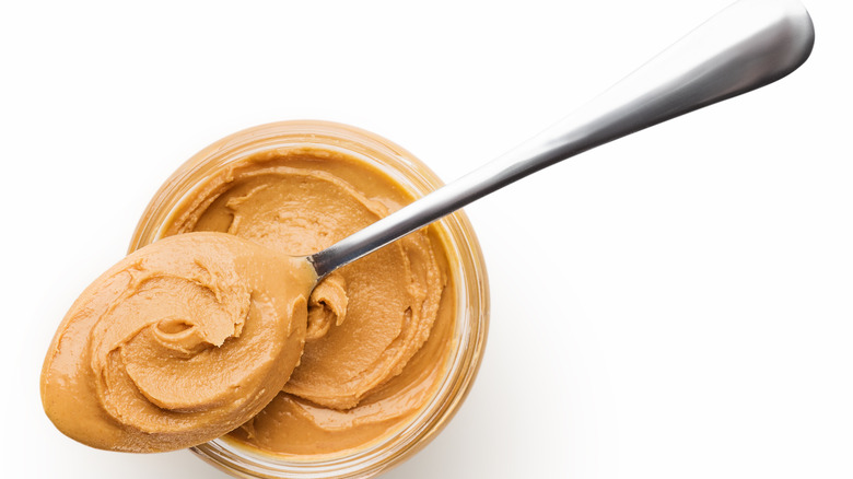 Peanut butter in glass jar and spoon isolated on white background