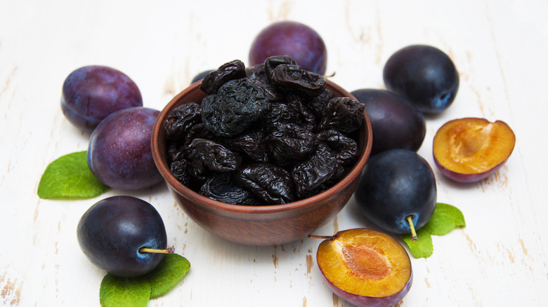 prunes in bowl surrounded by plums