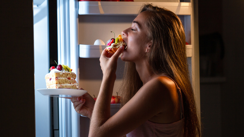A woman snacks on cake before bed