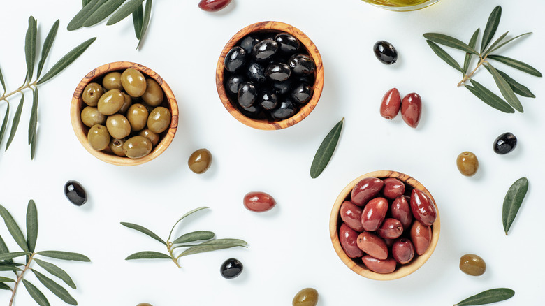 A variety of olives in wooden bowls against a white background decorated with olives and olive leaves