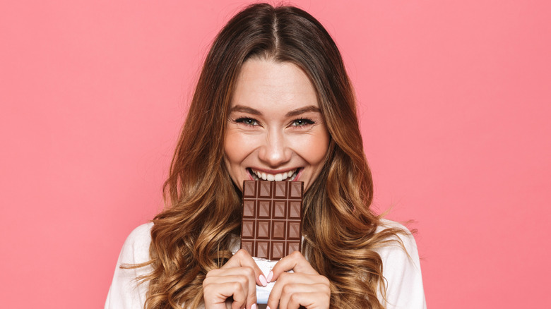 woman biting into a chocolate bar smiling and happy