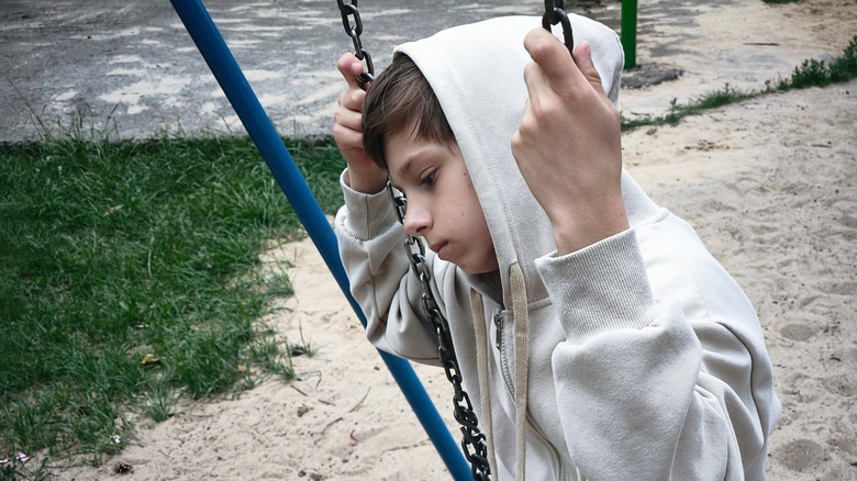 Sad child sitting alone on swing