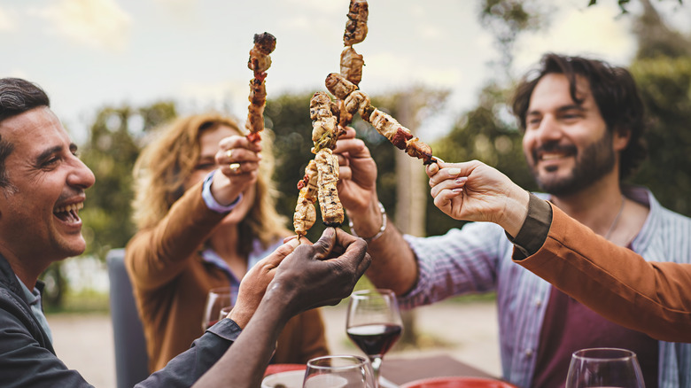 friends holding up barbecue sticks outdoors