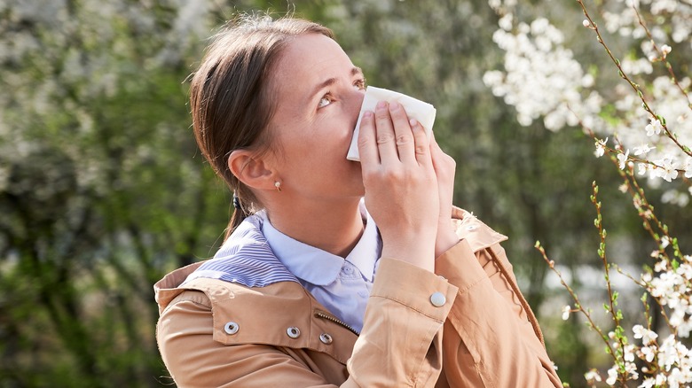 Woman outdoors sneezing near blossoming tree