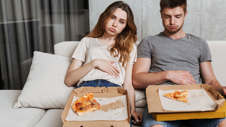 woman and man on sofa after eating too much pizza